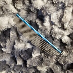 GroomBox moon comb for professional dog groomers with blue rounded spine and curved metal teeth on gray fur background